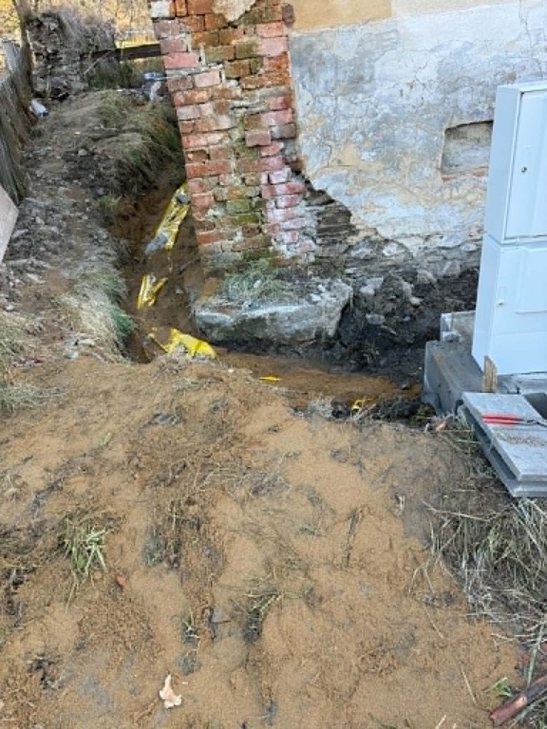 Výkop u staršího objektu při práci na potrubí